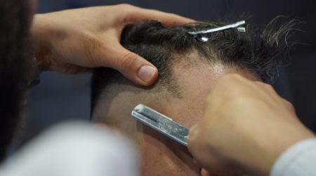 A barber using scissors to add texture to a man's thinning hair in a modern barbershop.