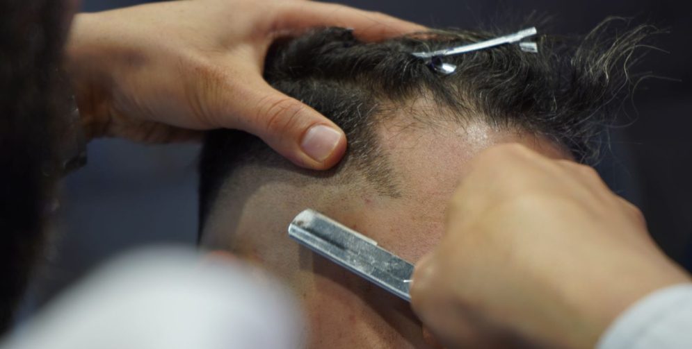 A barber using scissors to add texture to a man's thinning hair in a modern barbershop.