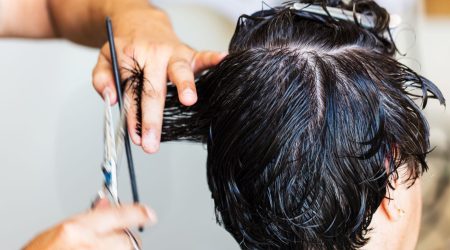 A barber using scissors to shape a male client's wavy hair inside a modern barbershop with mirrors and styling products