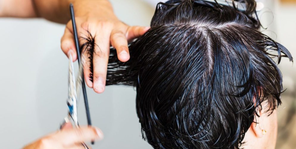 A barber using scissors to shape a male client's wavy hair inside a modern barbershop with mirrors and styling products