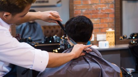 A barber uses scissors to shape the layered top of a wolf cut on a male client inside a modern barbershop.