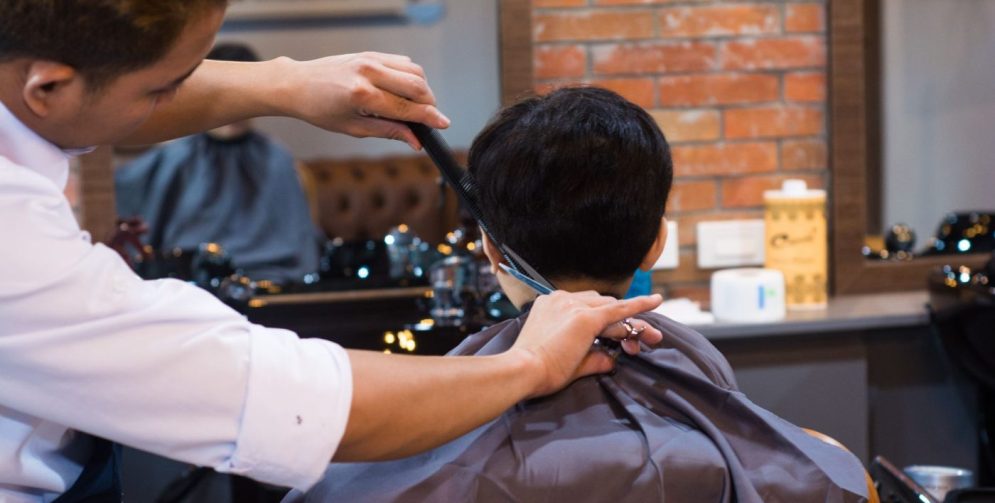 A barber uses scissors to shape the layered top of a wolf cut on a male client inside a modern barbershop.