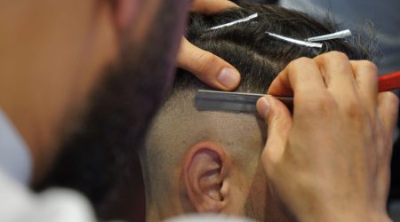 A barber uses scissors to cut the textured top of a man's French crop haircut inside a modern barbershop.
