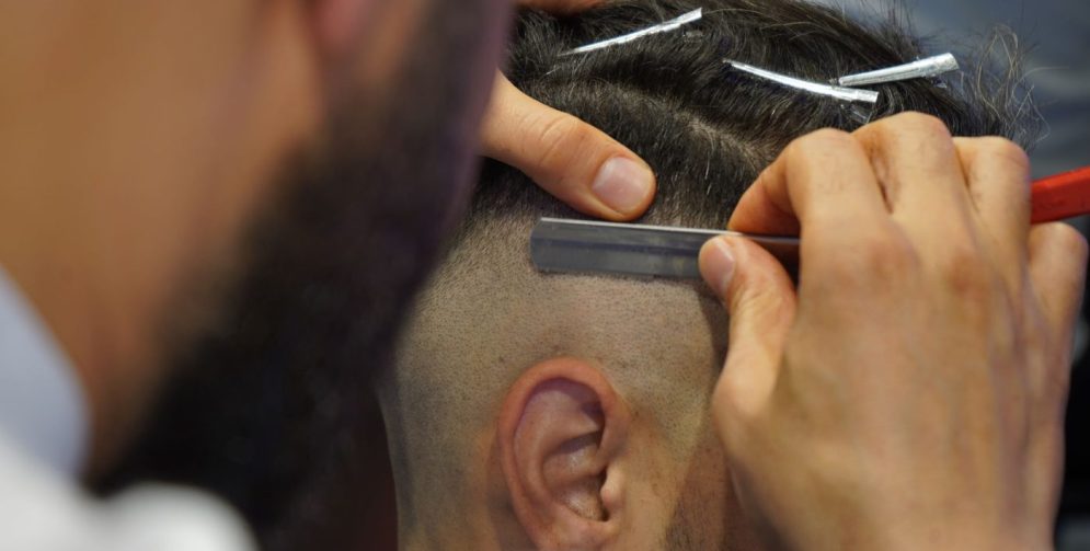 A barber uses scissors to cut the textured top of a man's French crop haircut inside a modern barbershop.