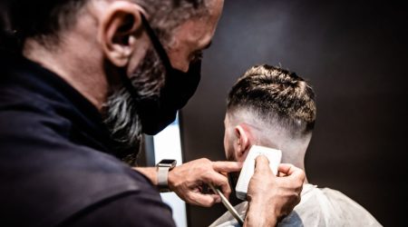 A man styles a voluminous pompadour haircut with a blow dryer in a bright bathroom.