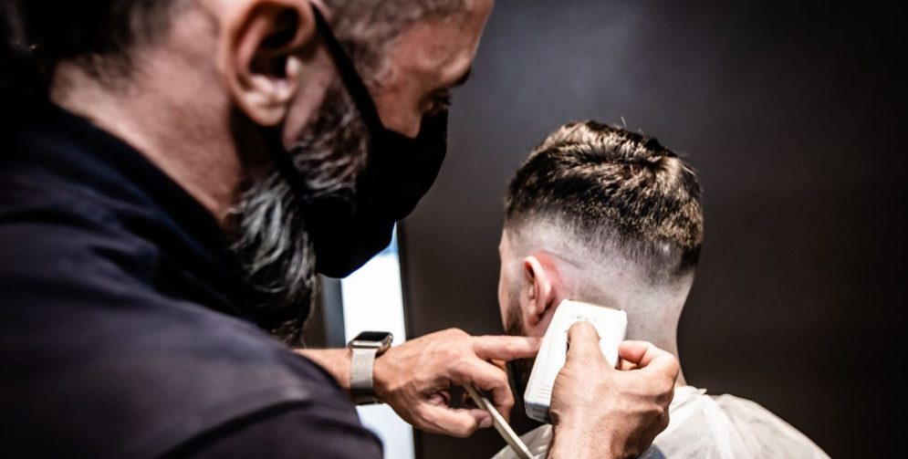 A man styles a voluminous pompadour haircut with a blow dryer in a bright bathroom.