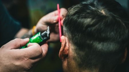 A man with a slick back hairstyle combing his hair back in a modern barbershop.