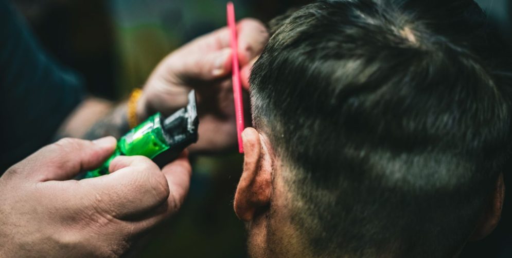 A man with a slick back hairstyle combing his hair back in a modern barbershop.