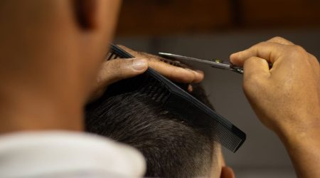 A male barber in a salon trims curtain bangs on a man, with the fringe parted in the middle and falling softly around th